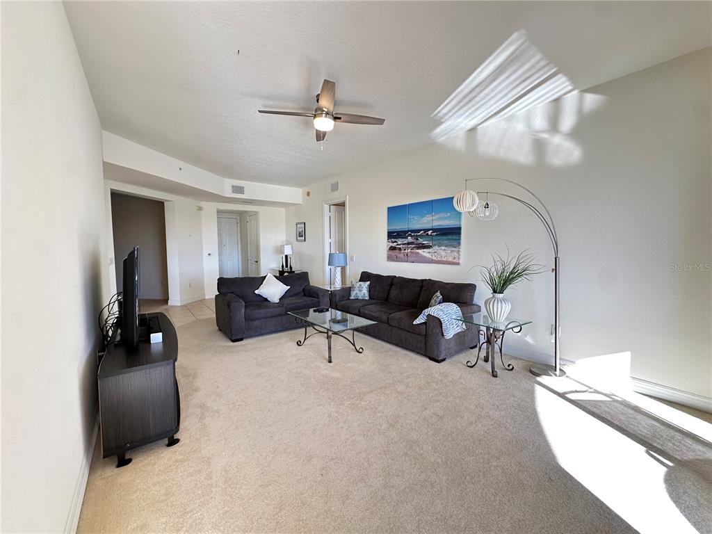 A living room features beige carpeting, two dark sofas, a glass coffee table, and a ceiling fan — 98 VIVANTE BOULEVARD UNIT 98315, PUNTA GORDA, FL