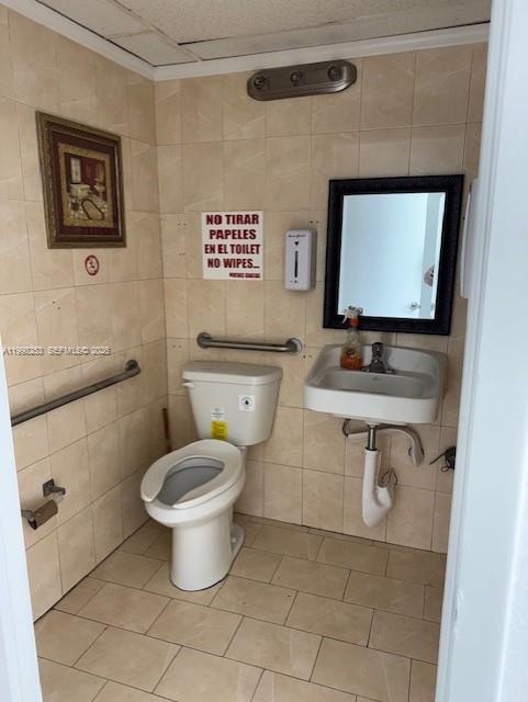 A small, tiled restroom features a toilet, a wall-mounted sink, and a framed picture — 5755 W Flagler St # 114, Miami FL 33144, MIAMI, FL