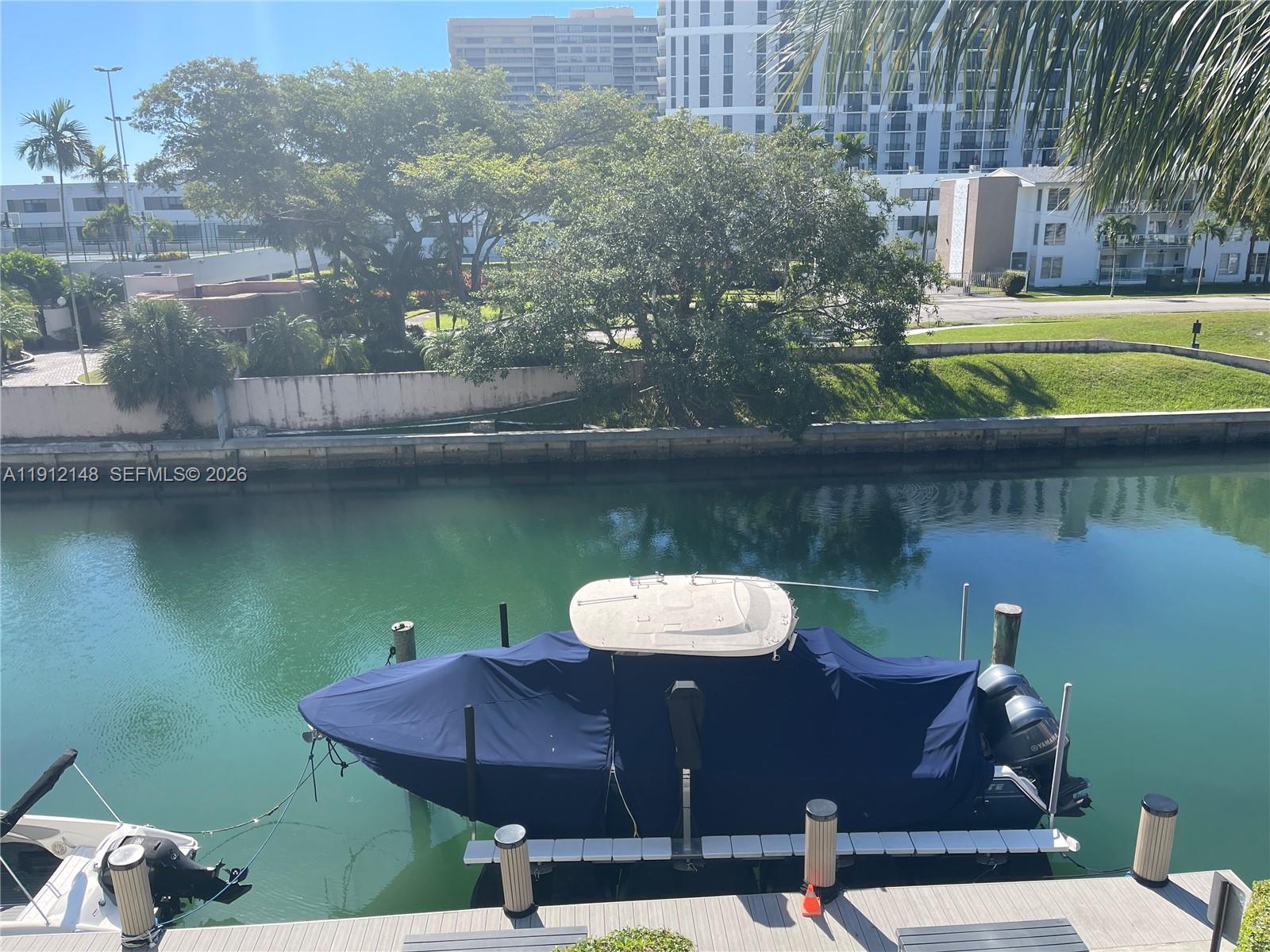 A boat covered in a blue tarp is docked in a canal near buildings — 1650 NE 115th St # 311, Miami FL 33181, MIAMI, FL