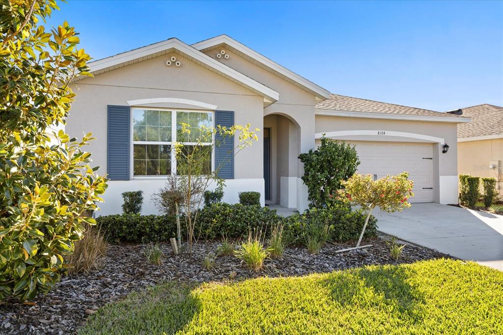 A single-story house with a beige stucco exterior, blue shutters, and an attached garage — 8104 PENROSE PLACE, WILDWOOD, FL