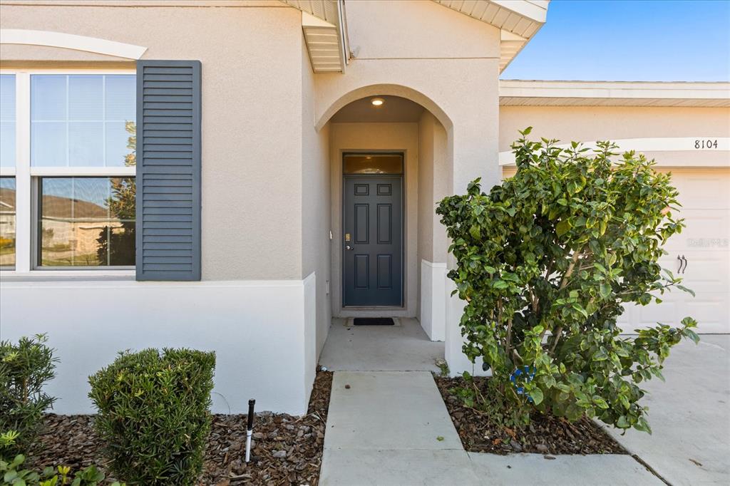 The exterior of a house features a gray front door, a walkway, and landscaping — 8104 PENROSE PLACE, WILDWOOD, FL