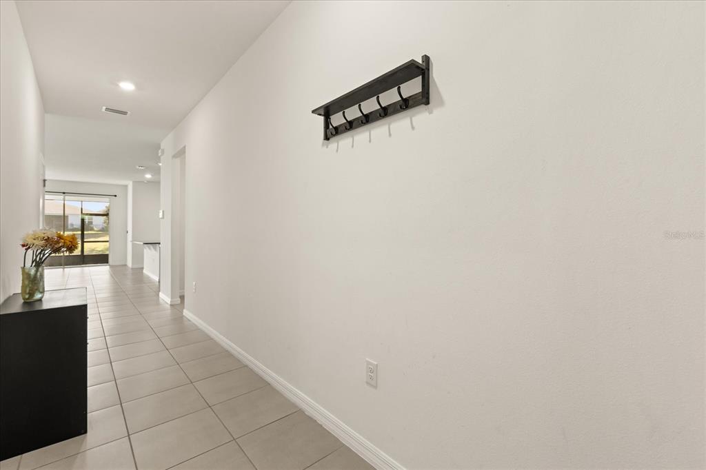 A hallway with tile flooring, a wall-mounted coat rack, and a view toward a patio — 8104 PENROSE PLACE, WILDWOOD, FL