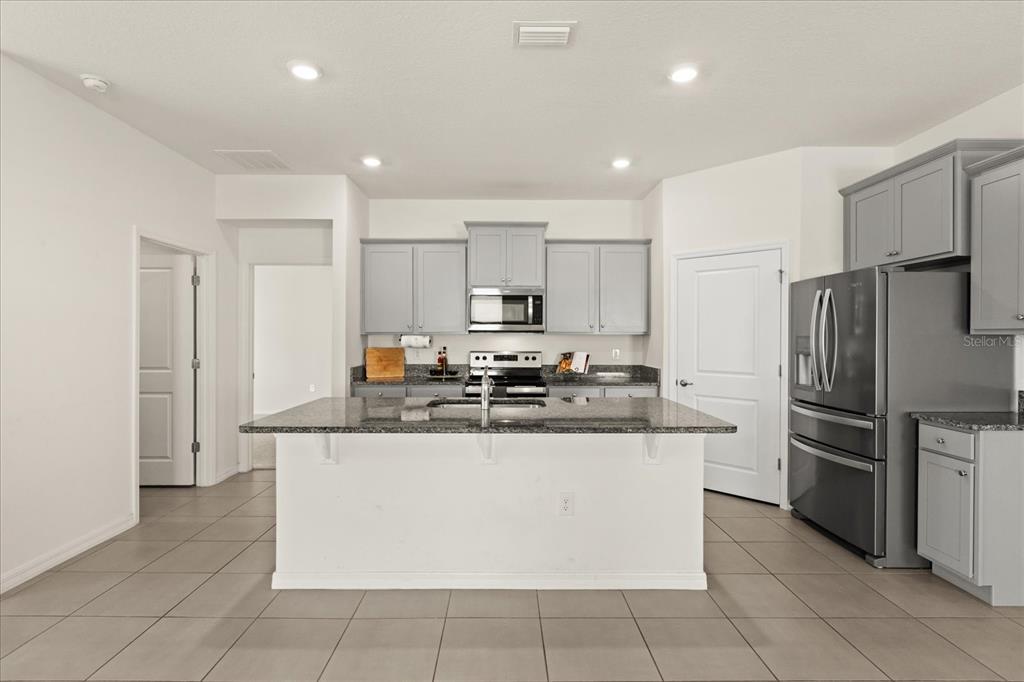 A kitchen features gray cabinets, stainless steel appliances, a granite-topped island, and tile flooring — 8104 PENROSE PLACE, WILDWOOD, FL
