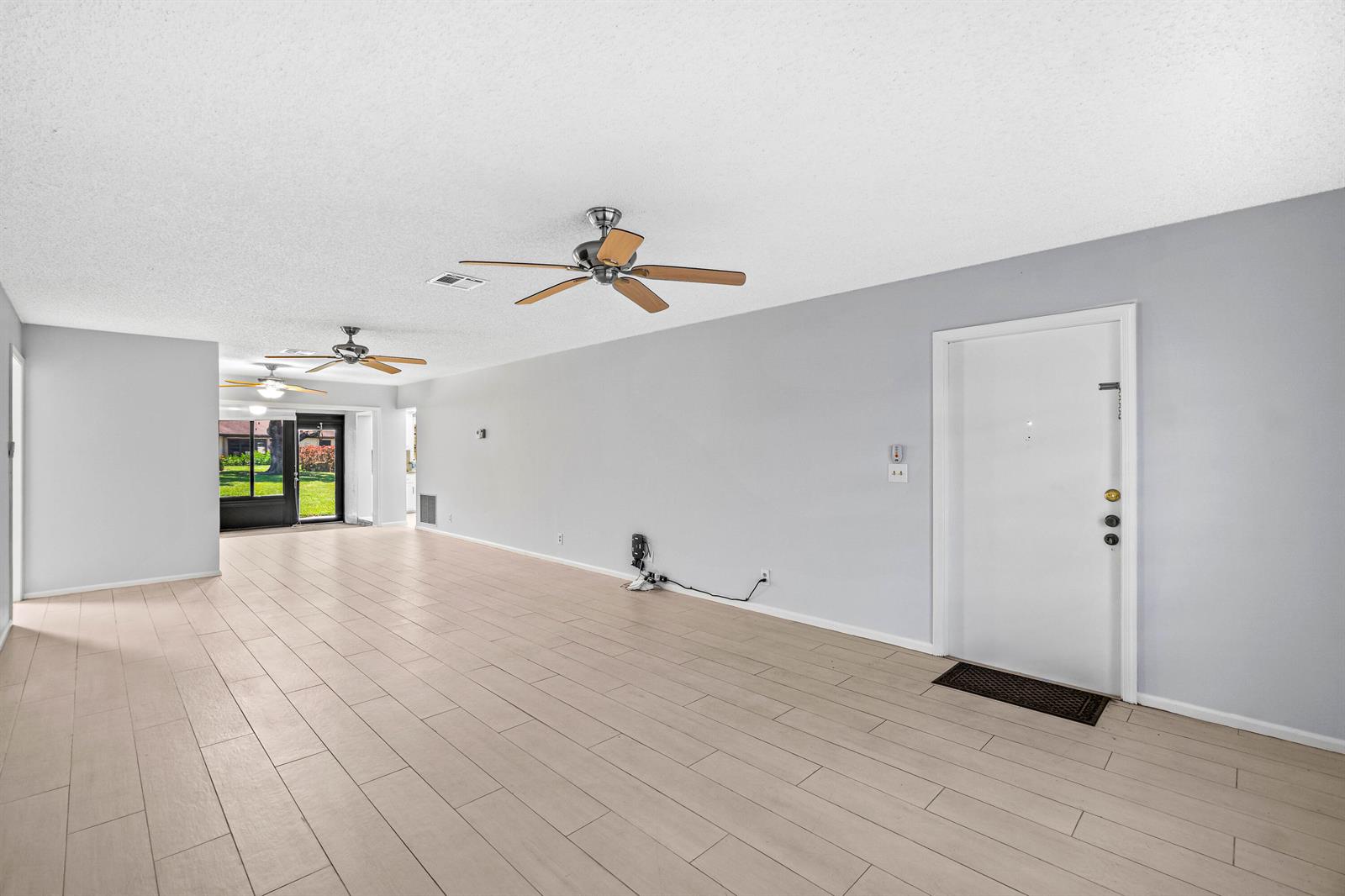An open living area features light wood-look tile flooring, gray walls, and two ceiling fans — 4897 Hawkwood Road # A, Boynton Beach FL 33436, BOYNTON BEACH, FL