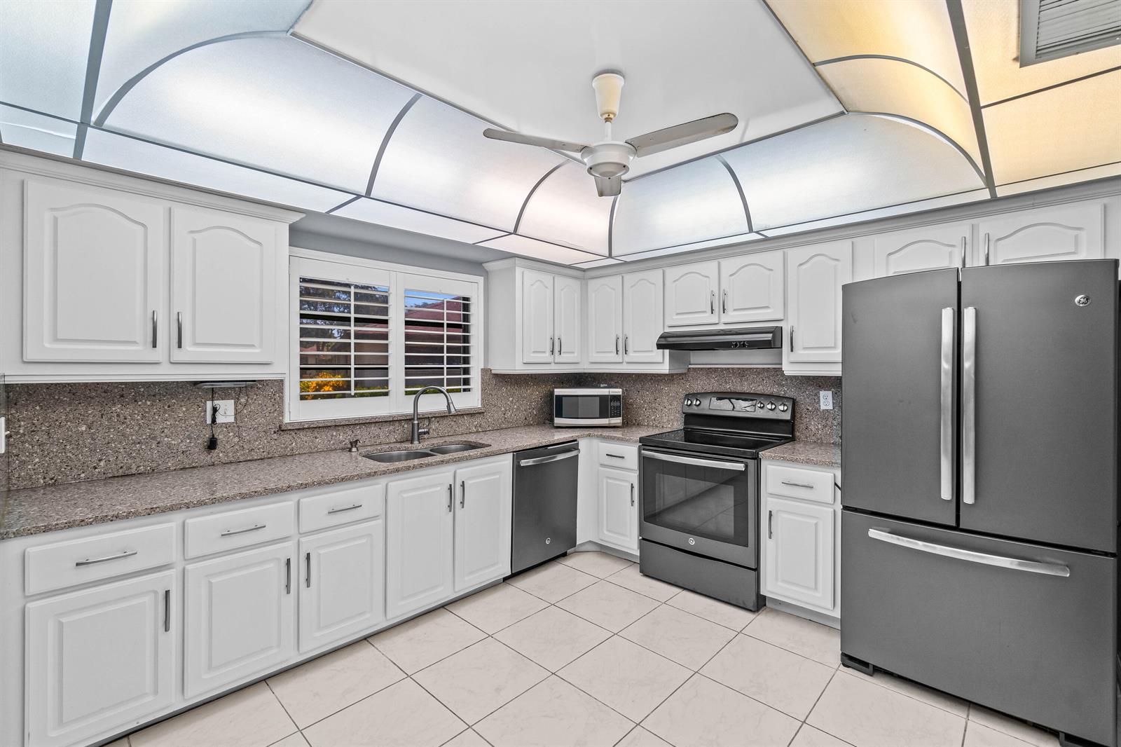 A kitchen features white cabinets, granite countertops, stainless steel appliances, and a vaulted ceiling light — 4897 Hawkwood Road # A, Boynton Beach FL 33436, BOYNTON BEACH, FL
