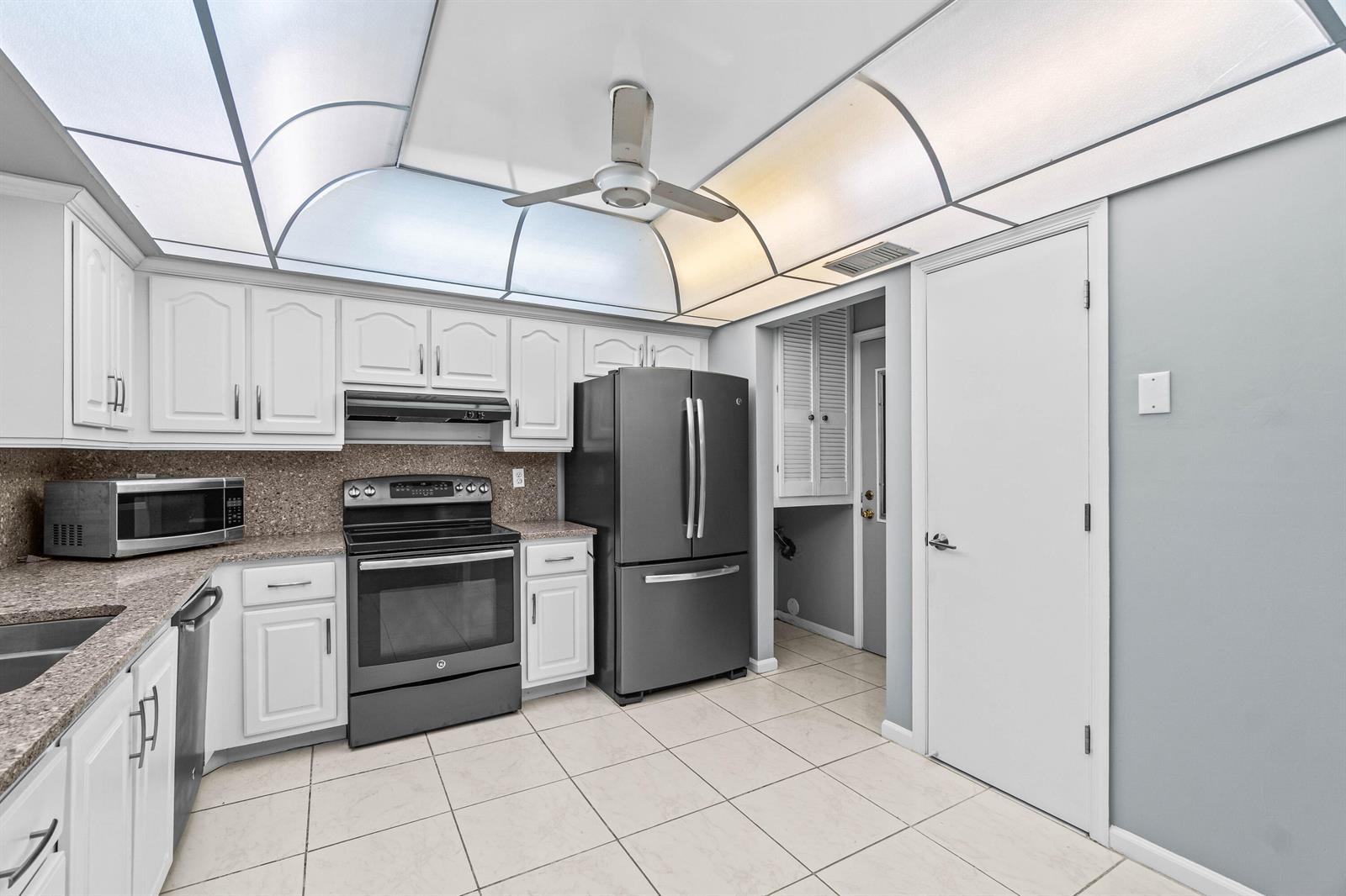 A kitchen features white cabinets, dark appliances, granite countertops, and a vaulted ceiling with lighting — 4897 Hawkwood Road # A, Boynton Beach FL 33436, BOYNTON BEACH, FL
