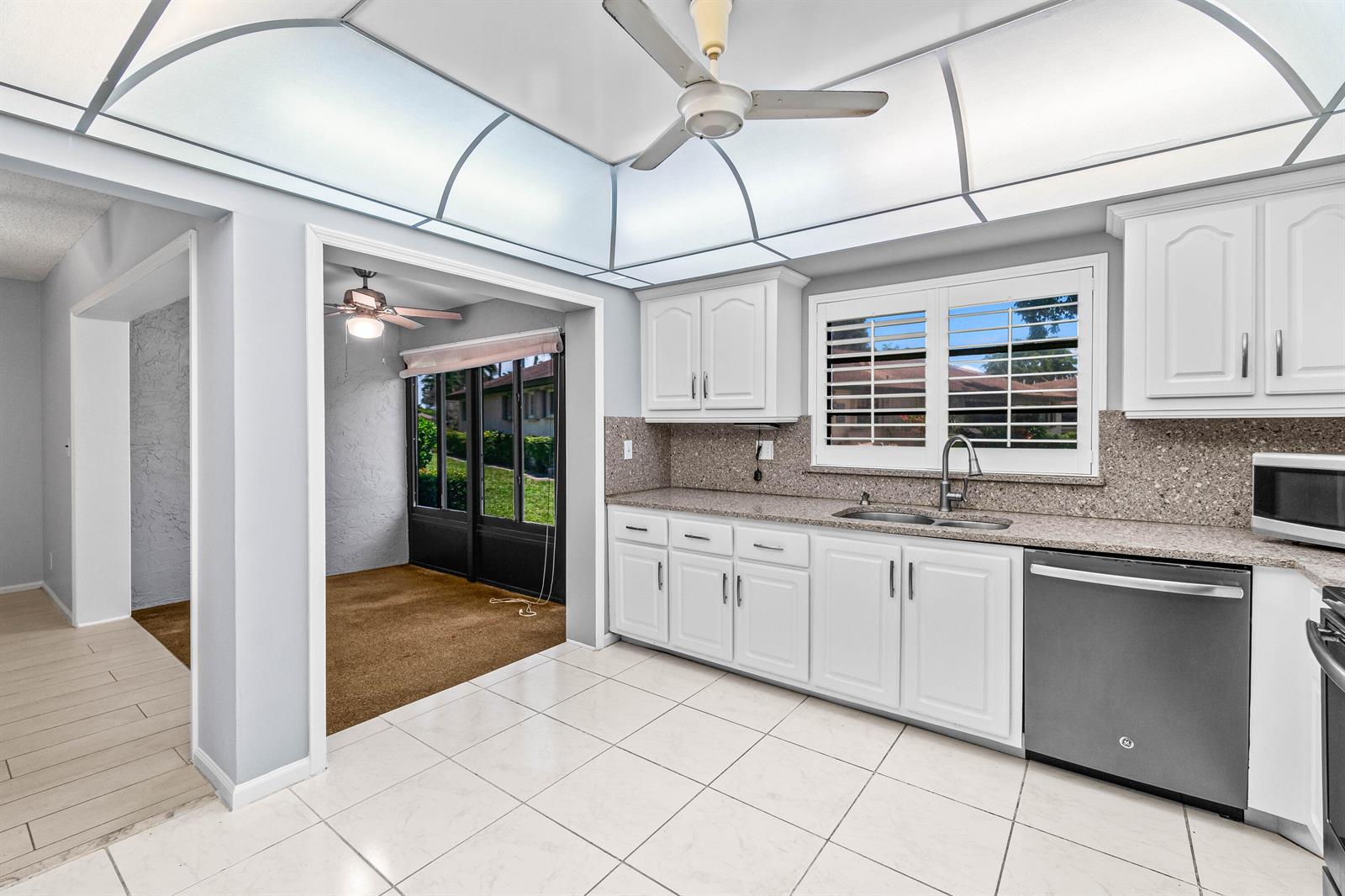 A kitchen with white cabinets, granite countertops, and a ceiling fan, adjacent to a sunroom — 4897 Hawkwood Road # A, Boynton Beach FL 33436, BOYNTON BEACH, FL