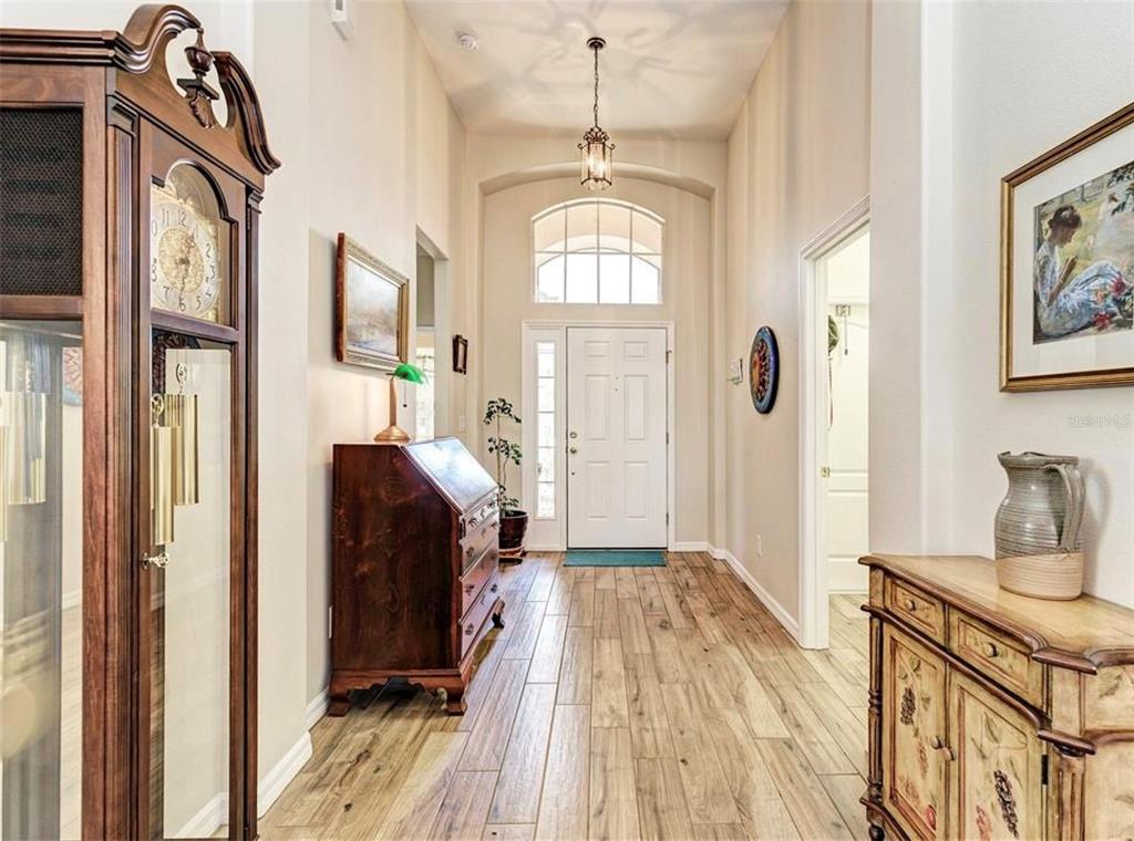 A foyer with wood-look tile flooring, a grandfather clock, and a white front door — 7106 50TH AVENUE CIRCLE E, PALMETTO, FL