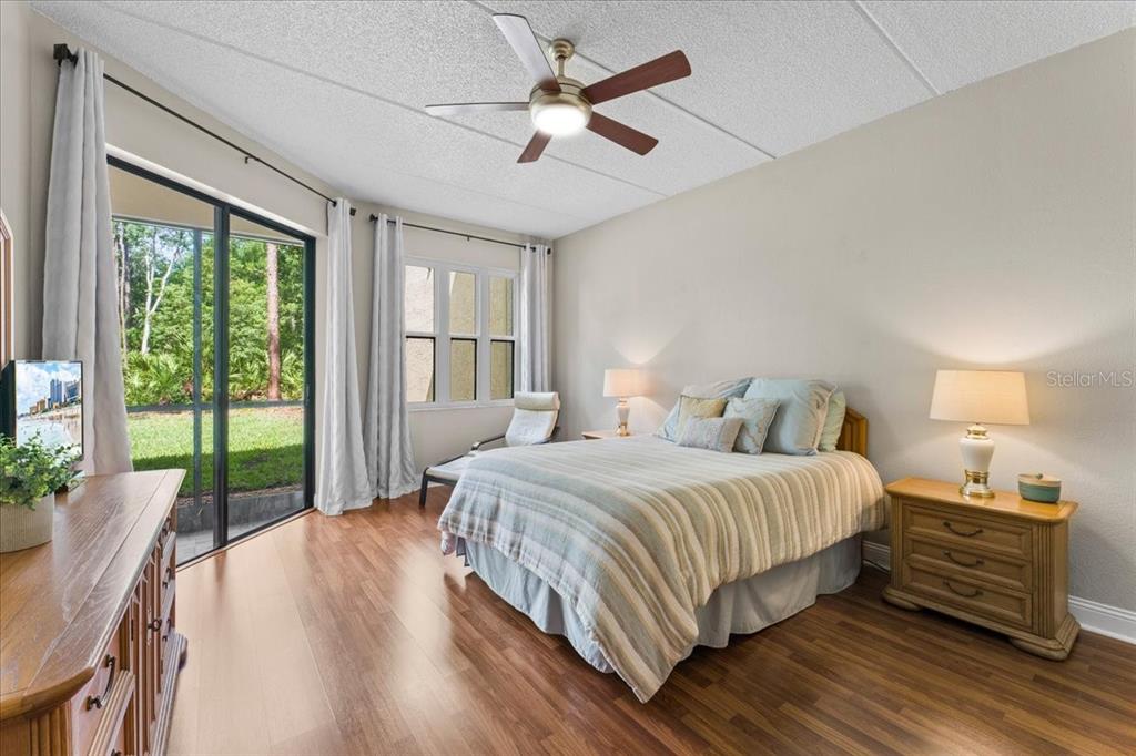 A bedroom features wood-look flooring, a ceiling fan, a queen bed, and a sliding glass door — 10 SHAMROCK WAY UNIT 10, OLDSMAR, FL
