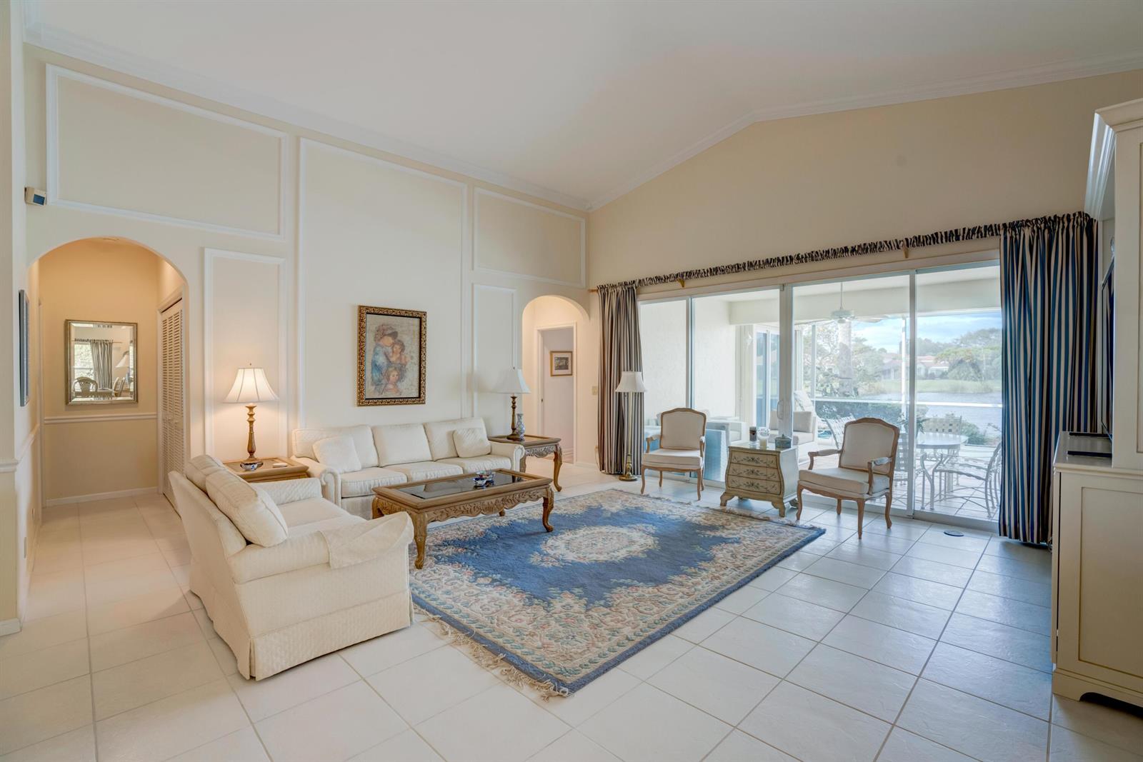 A living room with white tile floors, a blue area rug, and sliding glass doors — 3518 Lantern Bay Drive, Jupiter FL 33477, JUPITER, FL
