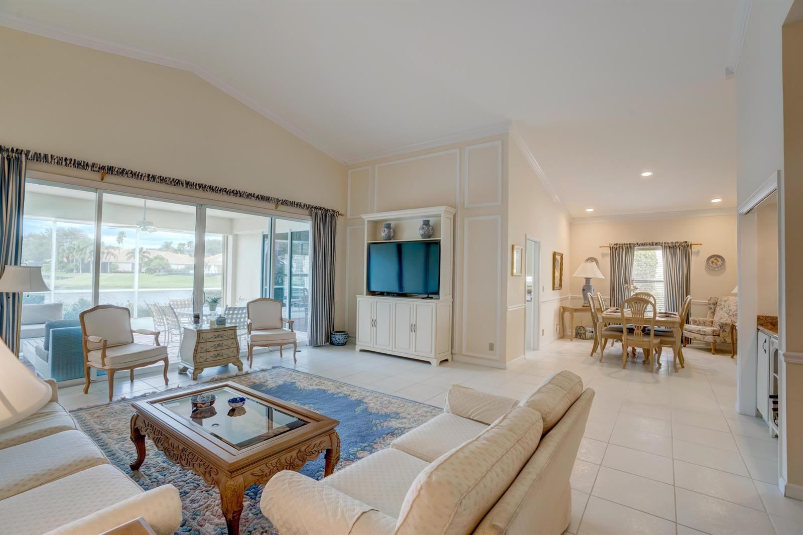 A living room with a vaulted ceiling, tile floors, and a dining area in the background — 3518 Lantern Bay Drive, Jupiter FL 33477, JUPITER, FL