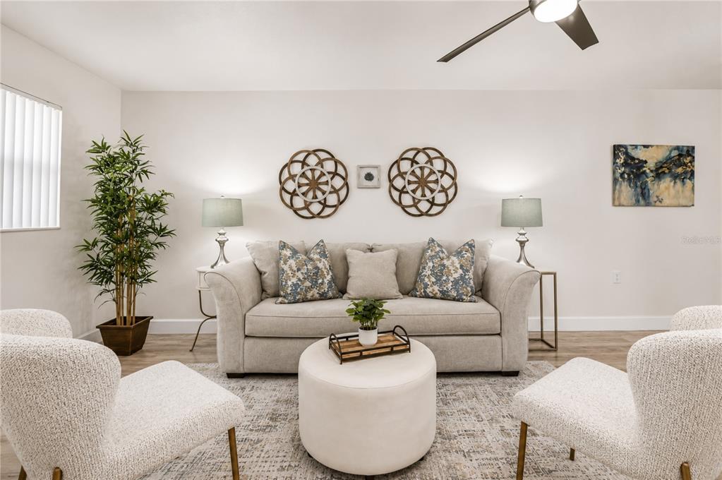 A living room features a beige sofa, two armchairs, a round ottoman, and wall decor — 10037 62ND TERRACE N UNIT 5, ST PETERSBURG, FL