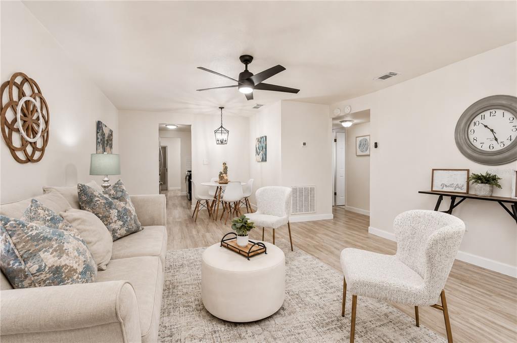 A living room with light wood flooring, a beige sofa, a round ottoman, and a dining area — 10037 62ND TERRACE N UNIT 5, ST PETERSBURG, FL