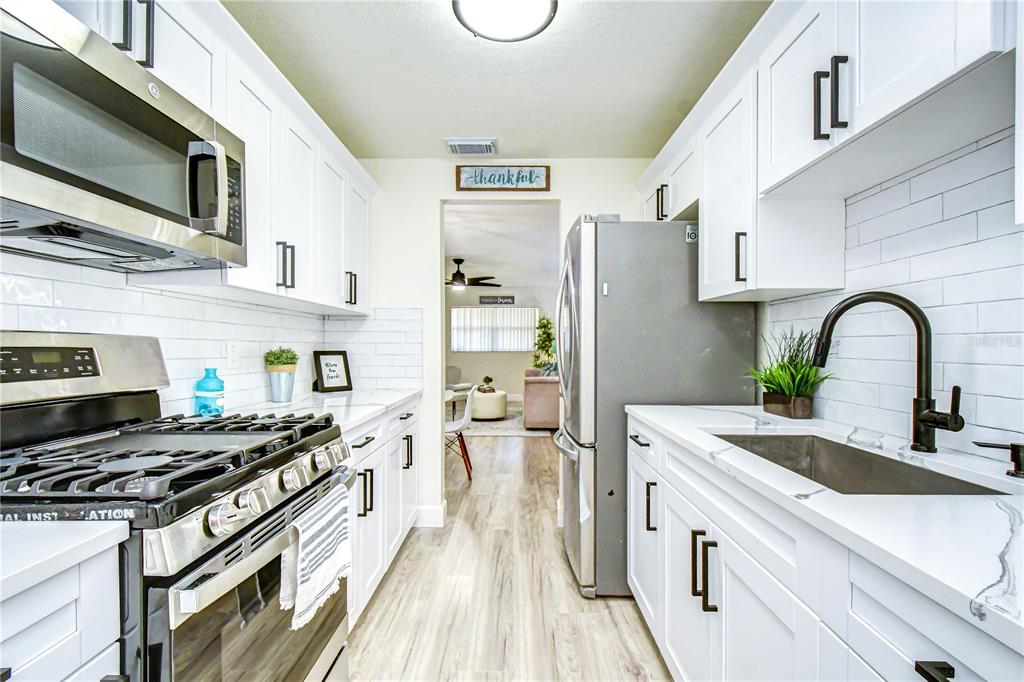 A narrow kitchen features white cabinets, stainless steel appliances, and a subway tile backsplash — 10037 62ND TERRACE N UNIT 5, ST PETERSBURG, FL