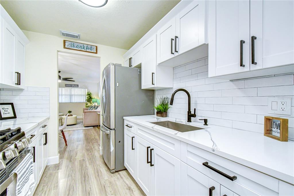 A galley kitchen features white cabinets, quartz countertops, a subway tile backsplash, and stainless appliances — 10037 62ND TERRACE N UNIT 5, ST PETERSBURG, FL