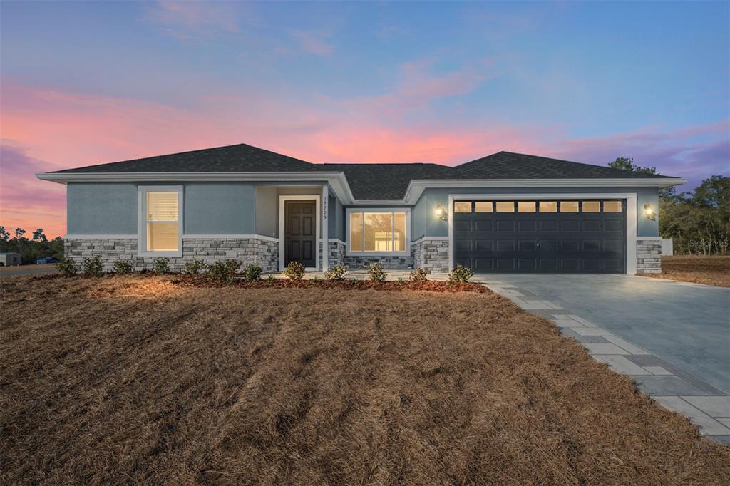 A single-story house with a blue exterior, stone accents, and a two-car garage at dusk — 6349 SW 153RD LANE ROAD, OCALA, FL