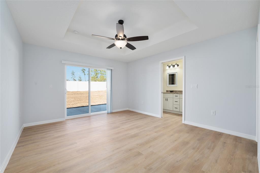 A bedroom with light wood-look flooring, a tray ceiling with a fan, and sliding doors — 6349 SW 153RD LANE ROAD, OCALA, FL