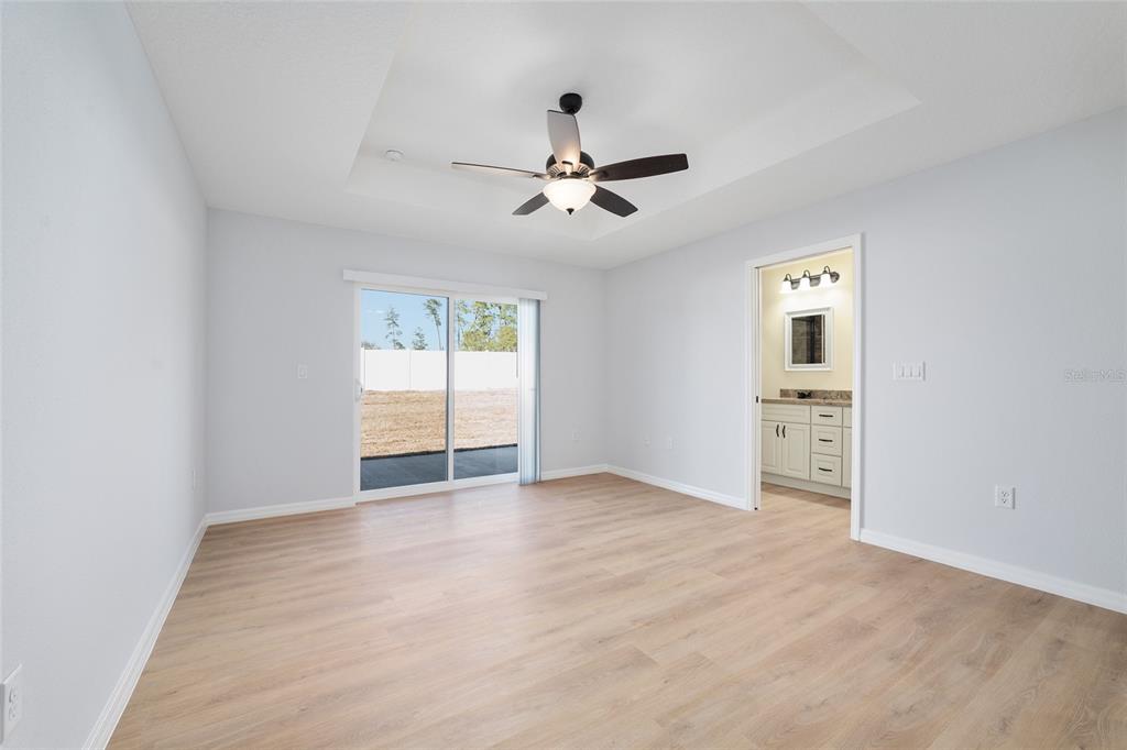A bedroom with light wood-look flooring, a tray ceiling with a fan, and an attached bathroom — 6349 SW 153RD LANE ROAD, OCALA, FL