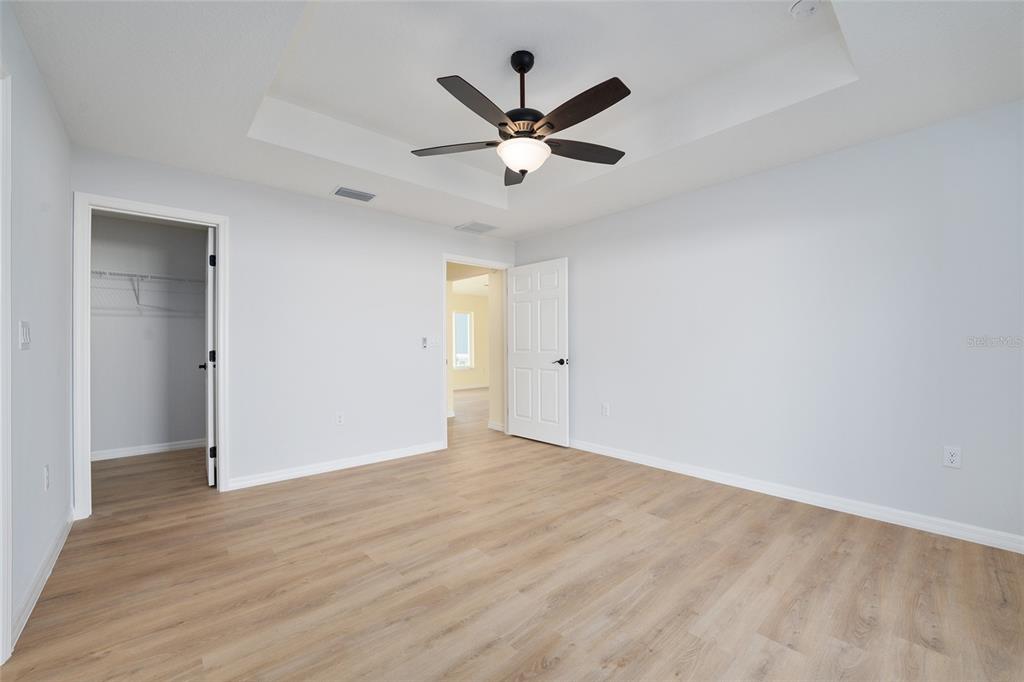 A bedroom with light gray walls, wood-look flooring, a tray ceiling, and a ceiling fan — 6349 SW 153RD LANE ROAD, OCALA, FL