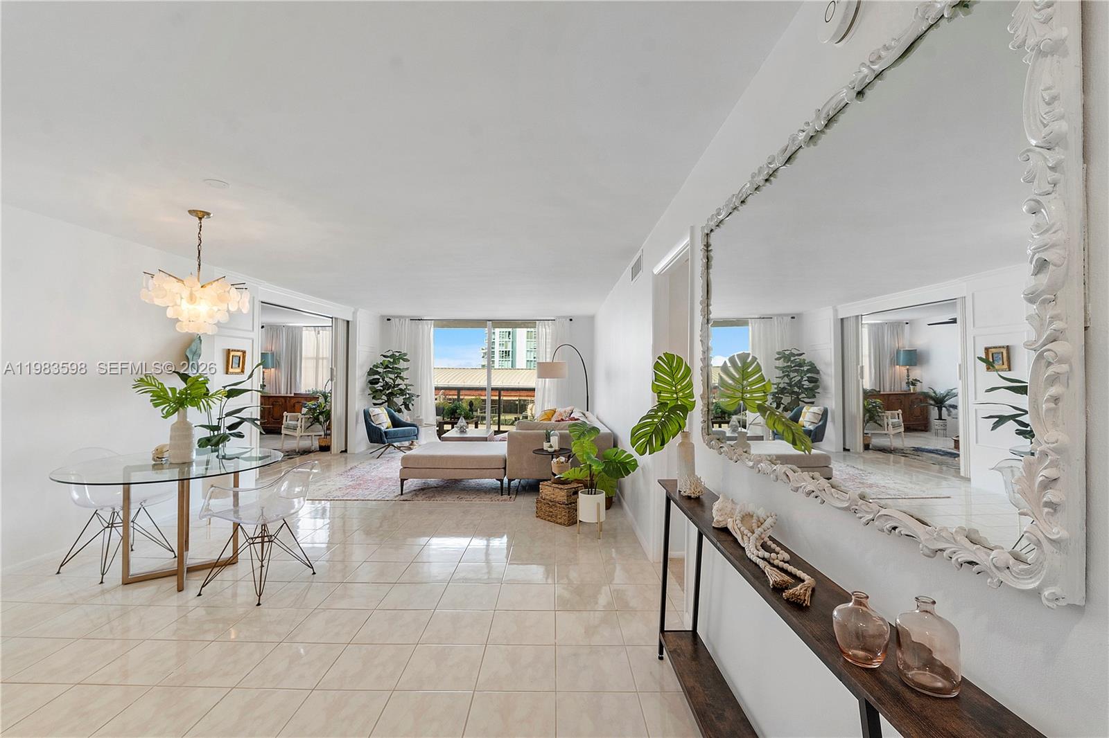A bright, open-concept living and dining area features tile floors, a large mirror, and balcony views — 6039 Collins Ave # 934, Miami Beach FL 33140, MIAMI BEACH, FL