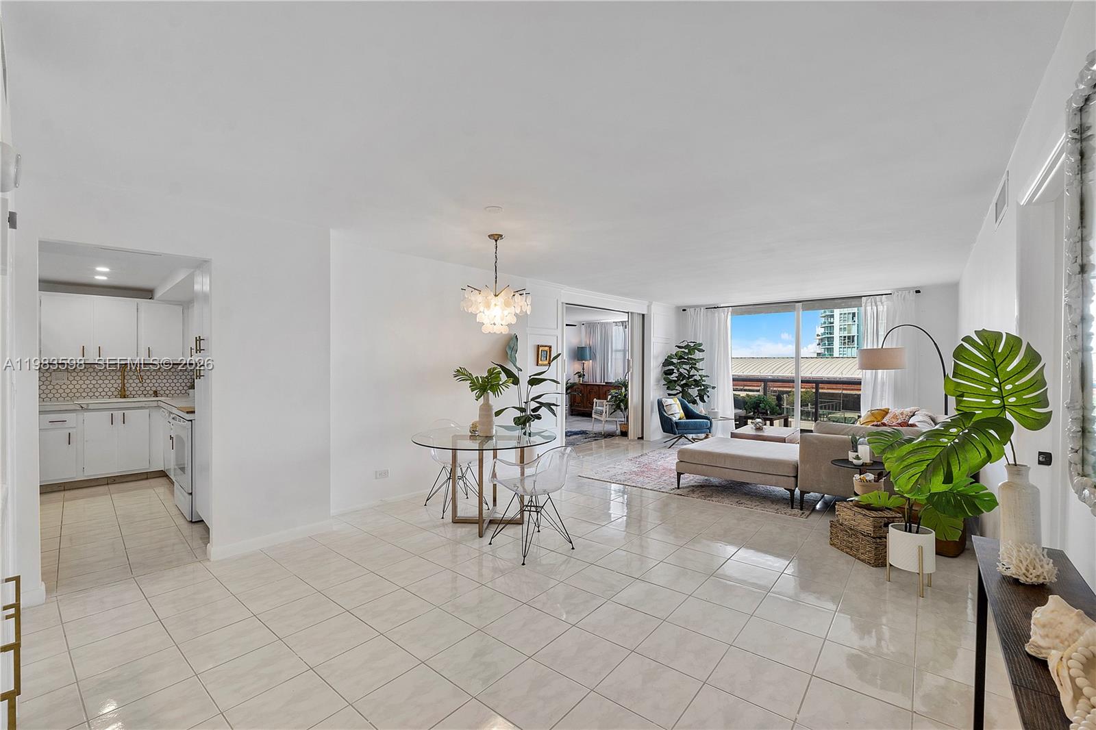 An open-concept living and dining area features white tile floors, a modern chandelier, and balcony access — 6039 Collins Ave # 934, Miami Beach FL 33140, MIAMI BEACH, FL