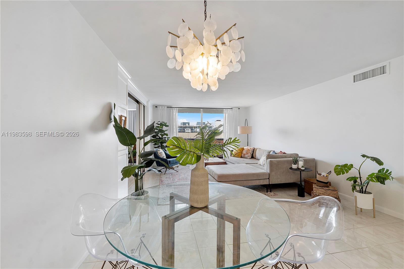 A bright living and dining area features a glass table, modern chandelier, and sectional sofa — 6039 Collins Ave # 934, Miami Beach FL 33140, MIAMI BEACH, FL
