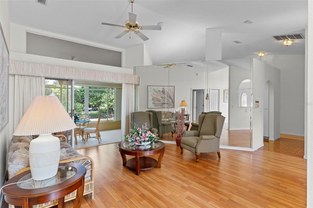 A living room features hardwood floors, a mirrored wall, and a sliding glass door — 3047 RIPPLING BROOK WAY, SPRING HILL, FL