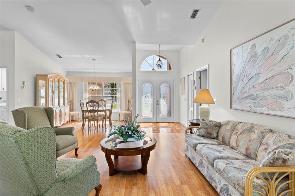 A living and dining area with wood flooring, vaulted ceilings, and a front entryway — 3047 RIPPLING BROOK WAY, SPRING HILL, FL