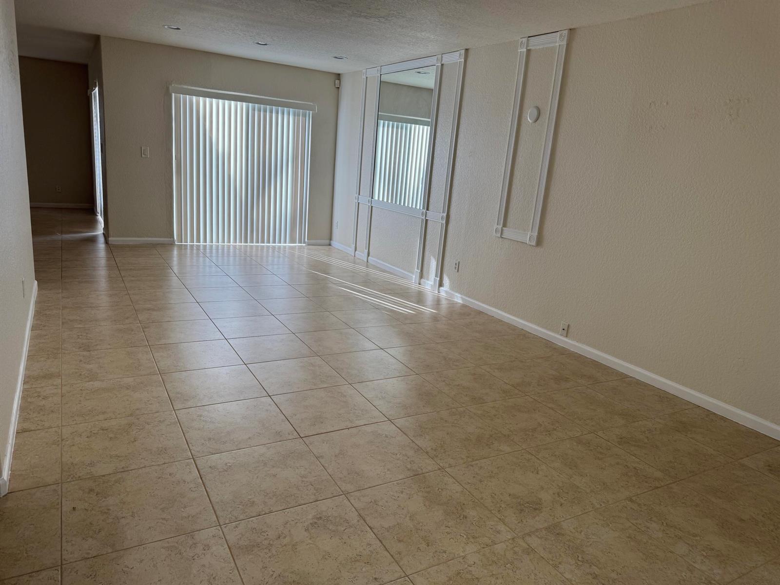 An empty room with beige tile flooring, a sliding glass door, and decorative wall molding — 3472 Commodore Court, West Palm Beach FL 33411, WEST PALM BEACH, FL