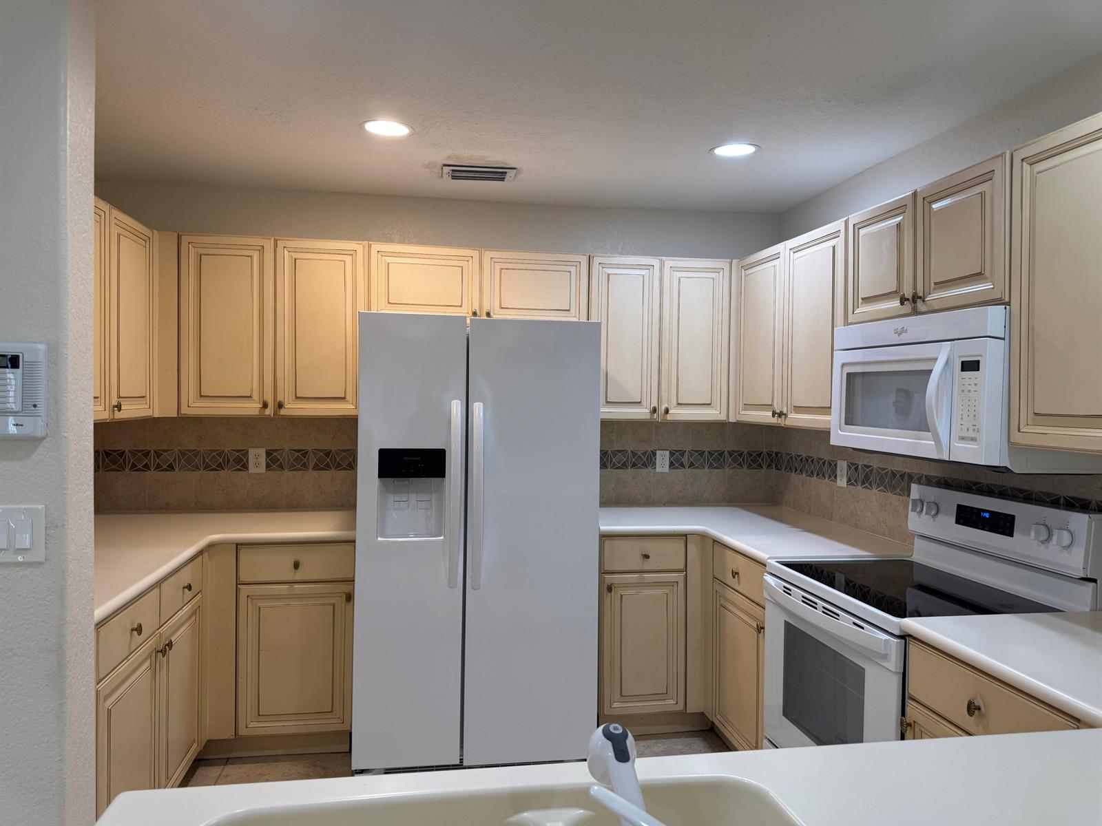 A kitchen features cream-colored cabinets, white appliances, and a tiled backsplash with decorative accents — 3472 Commodore Court, West Palm Beach FL 33411, WEST PALM BEACH, FL