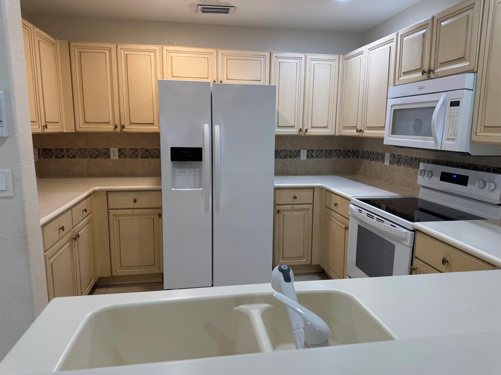 A kitchen features cream-colored cabinets, white appliances, and a double-basin sink on the counter — 3472 Commodore Court, West Palm Beach FL 33411, WEST PALM BEACH, FL