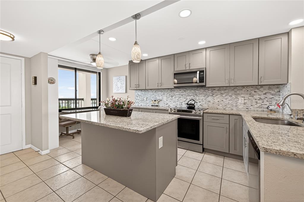 A kitchen features gray cabinets, granite countertops, a central island, and tile flooring — 9425 BLIND PASS ROAD UNIT 1103, ST PETE BEACH, FL