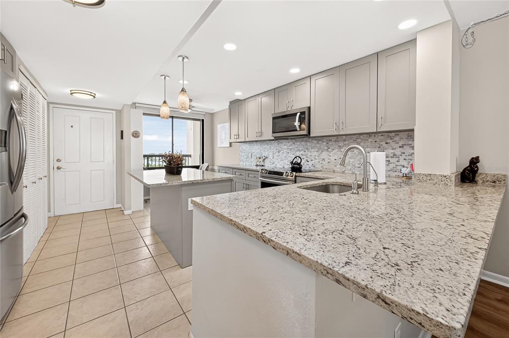 A kitchen features gray cabinets, granite countertops, a tiled backsplash, and a central island — 9425 BLIND PASS ROAD UNIT 1103, ST PETE BEACH, FL