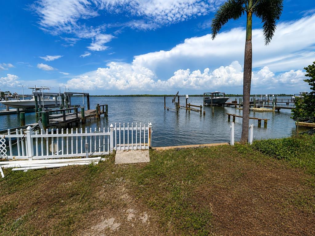 A white picket fence borders a grassy yard overlooking a bay with boat docks — 6111 BAYOU GRANDE BOULEVARD NE, ST PETERSBURG, FL