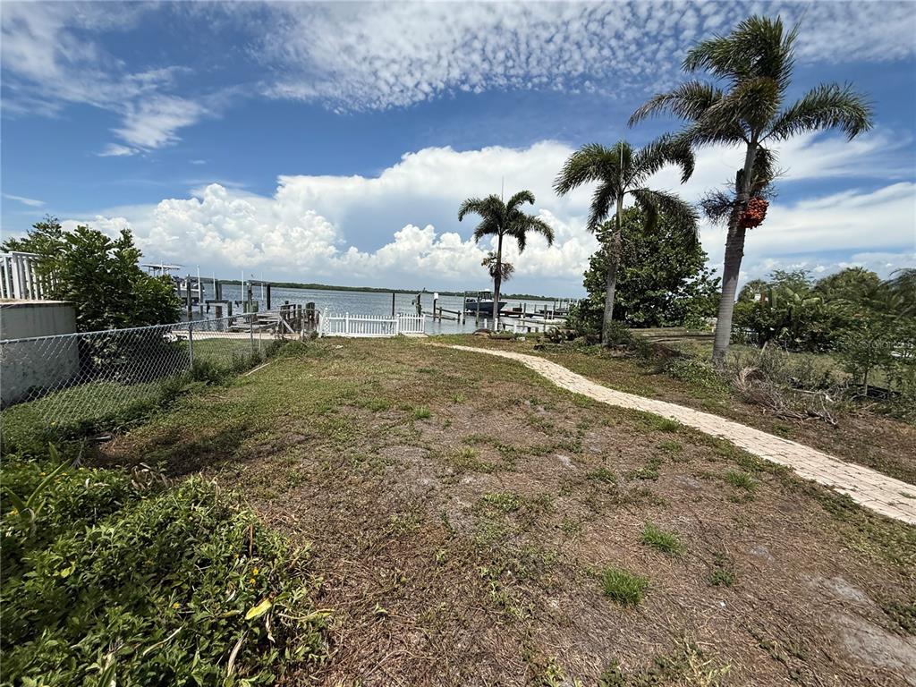A grassy yard leads to a white fence, boat docks, and palm trees by the water — 6111 BAYOU GRANDE BOULEVARD NE, ST PETERSBURG, FL