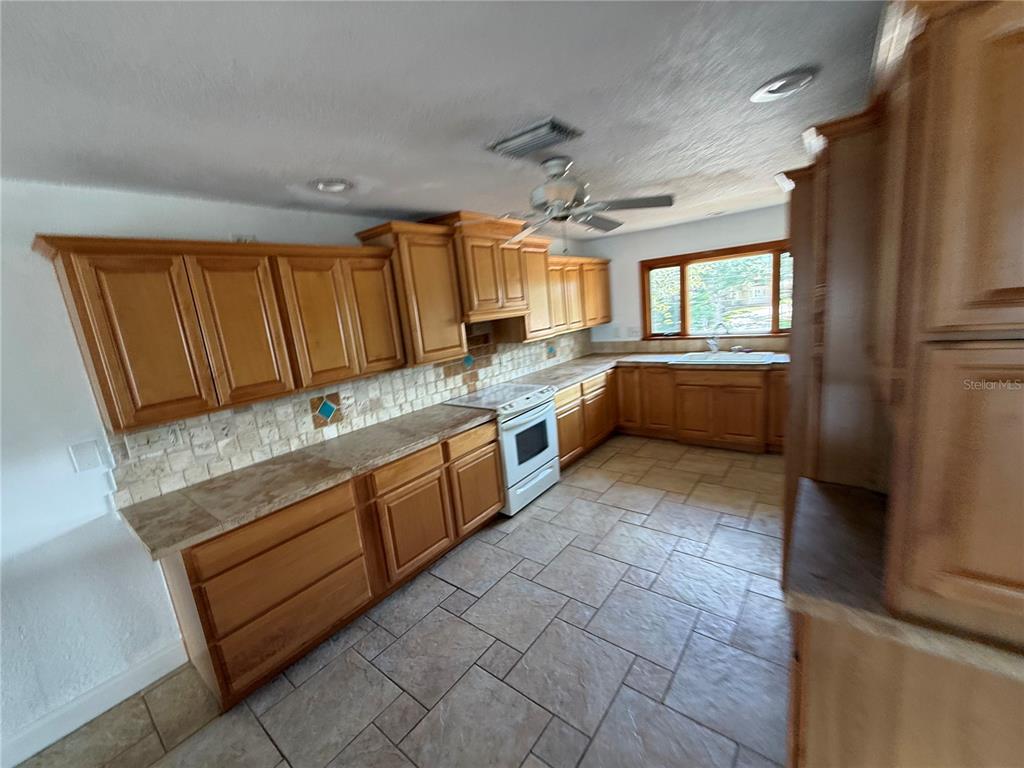 A kitchen features wood cabinets, tile countertops, a white stove, and tiled flooring — 6111 BAYOU GRANDE BOULEVARD NE, ST PETERSBURG, FL