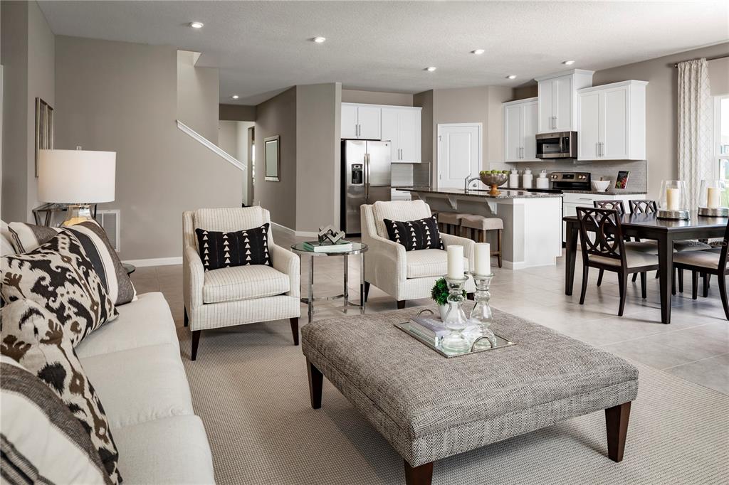 An open-concept living room and kitchen featuring white cabinetry, neutral furniture, and tile flooring — 1039 OCEAN LODGE ROAD, LADY LAKE, FL