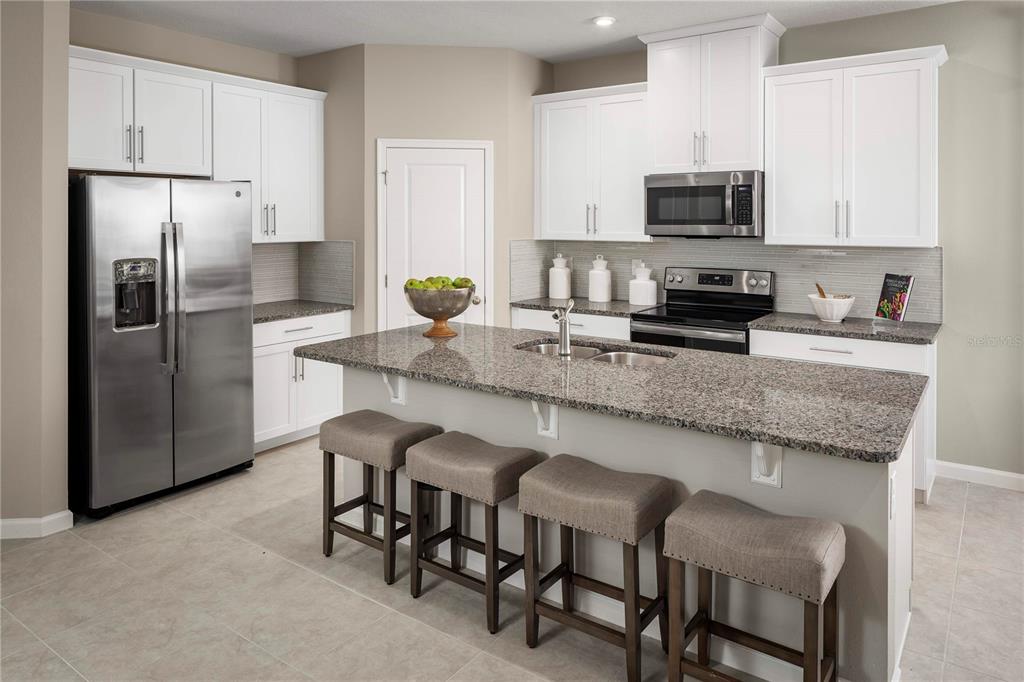 A kitchen features white cabinets, granite countertops, a stainless steel refrigerator, and a breakfast island — 1039 OCEAN LODGE ROAD, LADY LAKE, FL