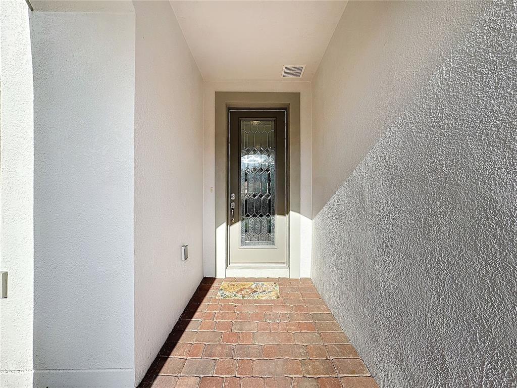 A covered entryway features a brick floor, white stucco walls, and a glass-paneled front door — 362 VIA TORRENTE DRIVE, KISSIMMEE, FL