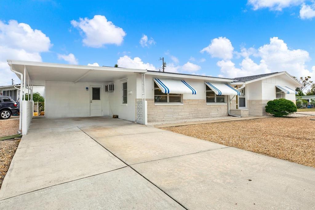 A single-story house with a white exterior, stone accents, blue-striped awnings, and a concrete carport — 1617 DERRICK STREET, HOLIDAY, FL