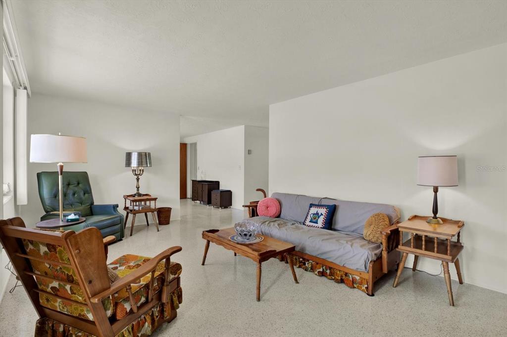 A living room features a wooden rocking chair, a sofa, and light-colored terrazzo flooring — 1617 DERRICK STREET, HOLIDAY, FL