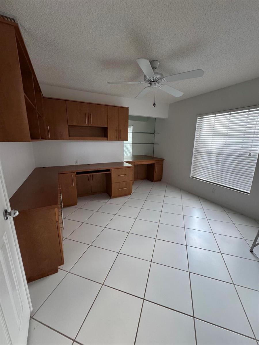 A home office features built-in wooden cabinetry, a desk, tile flooring, and a ceiling fan — 6113 Greenspointe Drive # 10, Boynton Beach FL 33437, BOYNTON BEACH, FL