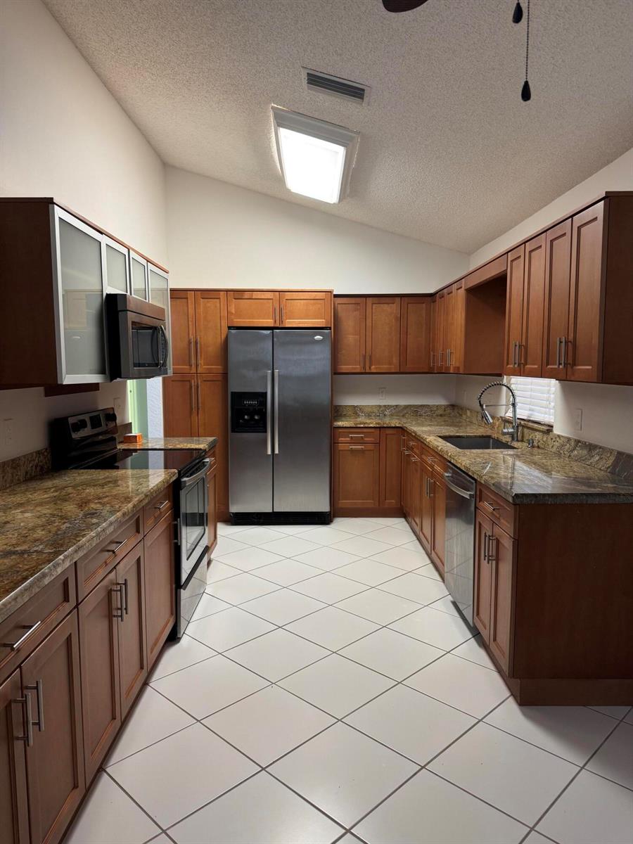 A kitchen with wood cabinets, granite countertops, stainless steel appliances, and white tiled flooring — 6113 Greenspointe Drive # 10, Boynton Beach FL 33437, BOYNTON BEACH, FL