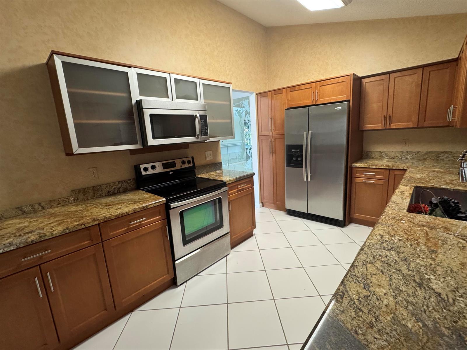 A kitchen features wood cabinets, granite countertops, stainless steel appliances, and white tile flooring — 6113 Greenspointe Drive # 10, Boynton Beach FL 33437, BOYNTON BEACH, FL