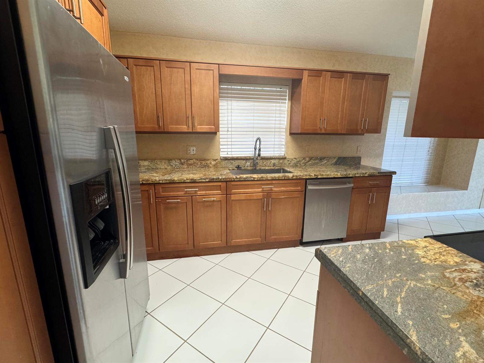 A kitchen features wood cabinets, granite countertops, stainless steel appliances, and white tile flooring — 6113 Greenspointe Drive # 10, Boynton Beach FL 33437, BOYNTON BEACH, FL