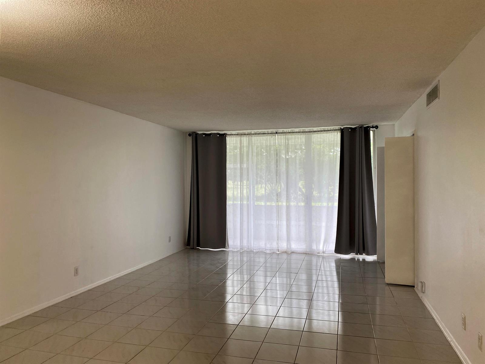 An empty living room features light-colored floor tiles, white walls, and floor-to-ceiling sliding glass doors — 2751 S Palm Aire Drive # 107, Pompano Beach FL 33069, POMPANO BEACH, FL
