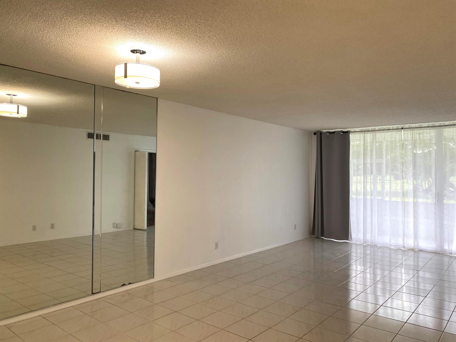 An empty room with tiled floors, a mirrored wall, and floor-to-ceiling curtains — 2751 S Palm Aire Drive # 107, Pompano Beach FL 33069, POMPANO BEACH, FL
