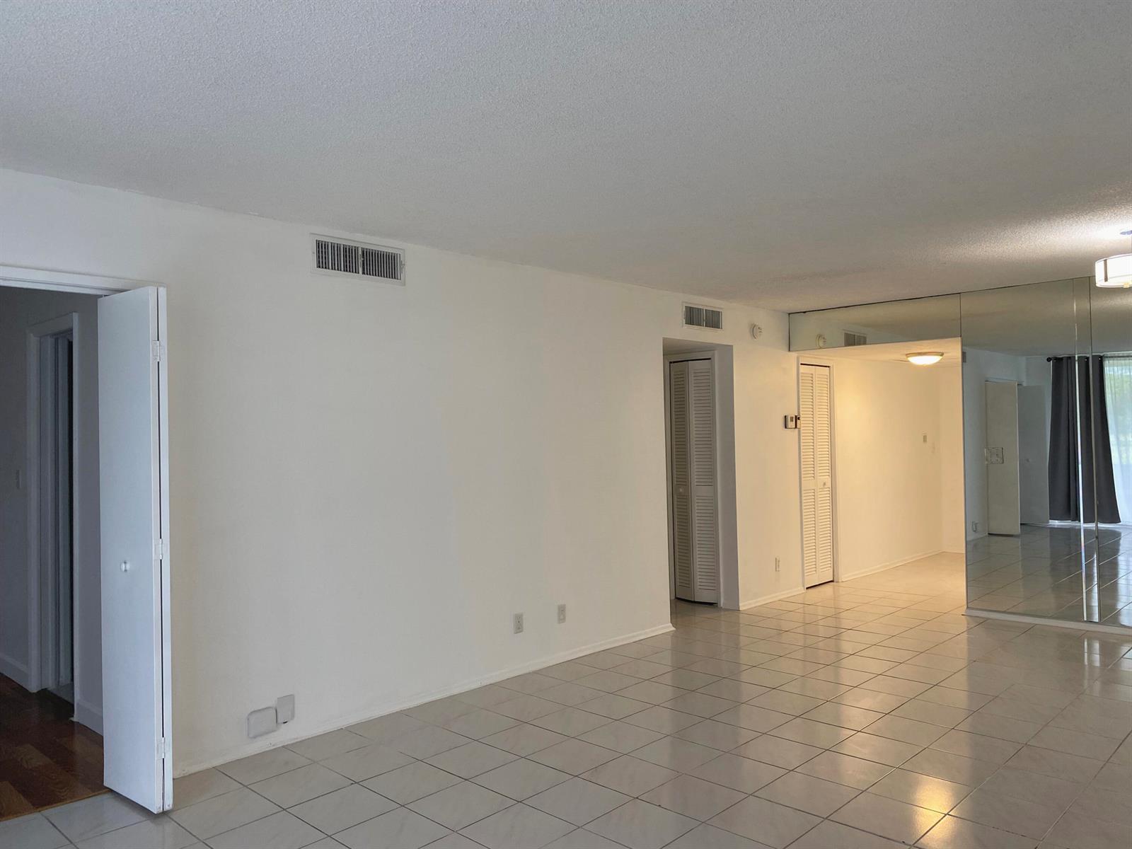 An empty room with white walls, tiled floors, and a mirrored wall section — 2751 S Palm Aire Drive # 107, Pompano Beach FL 33069, POMPANO BEACH, FL