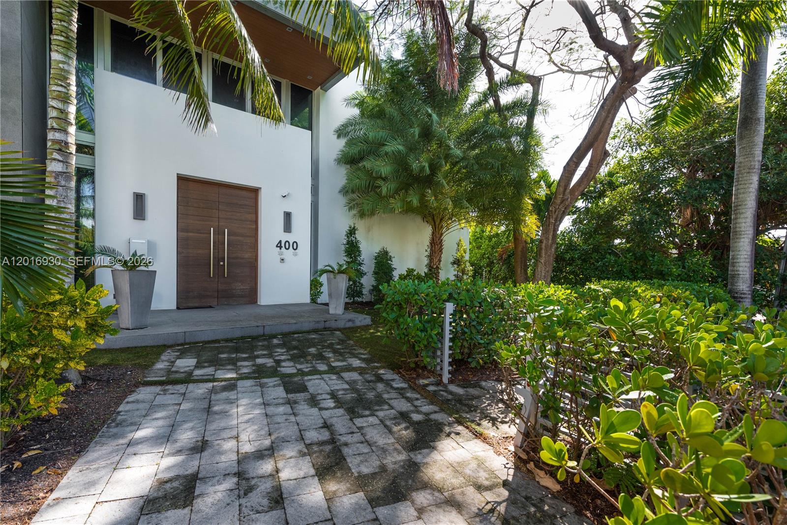 A modern white house features a large wooden double door entrance and a paved walkway — 400 Tamarind Dr, Hallandale Beach FL 33009, HALLANDALE BEACH, FL