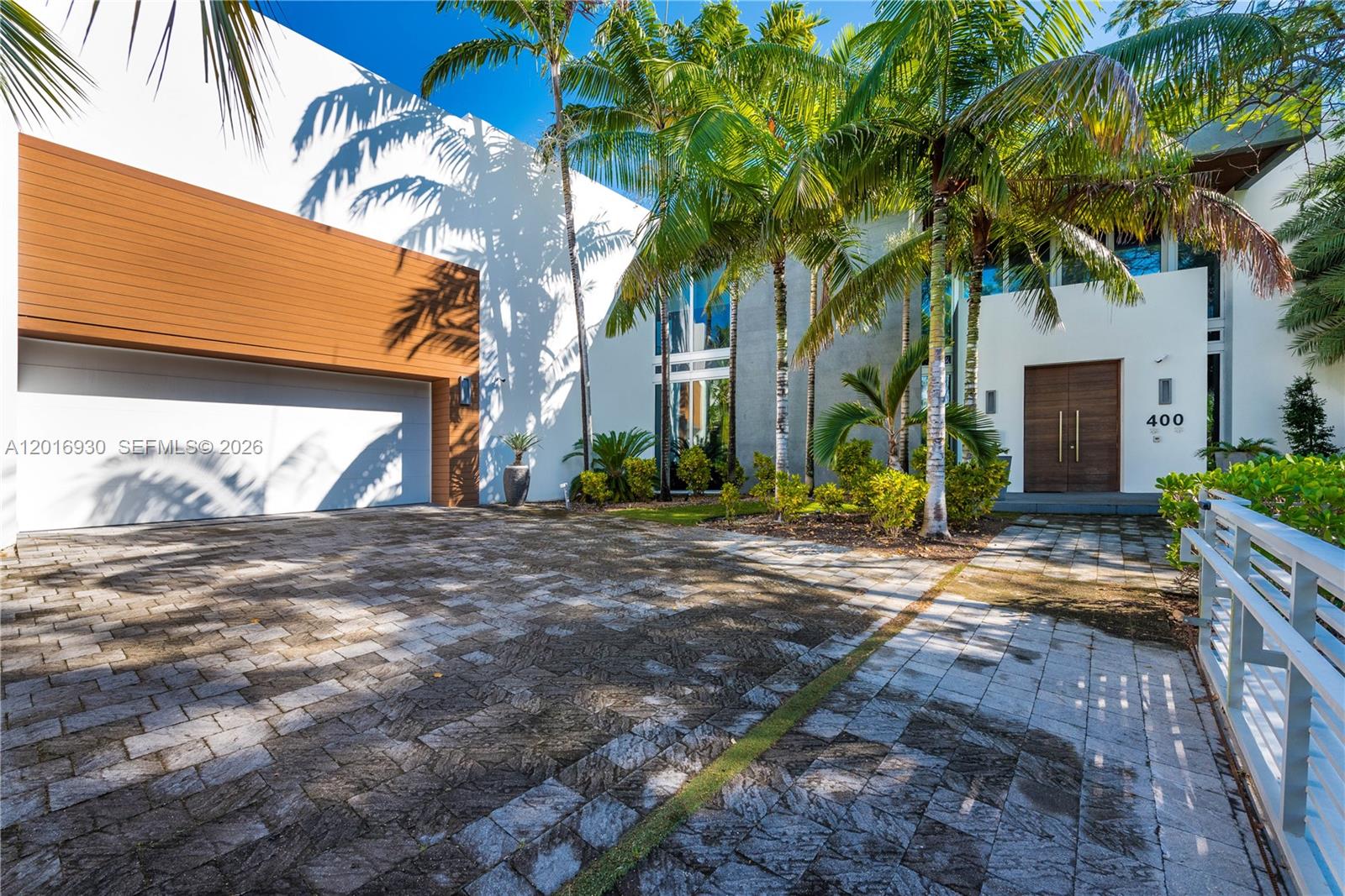 A modern house exterior features a white facade, wood accents, palm trees, and a paved driveway — 400 Tamarind Dr, Hallandale Beach FL 33009, HALLANDALE BEACH, FL